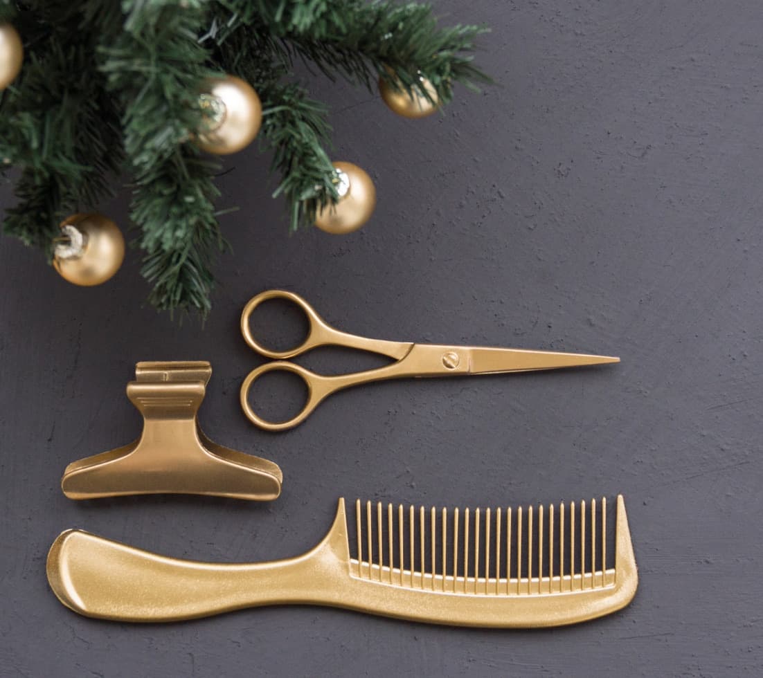 A gold comb, hair clip, and pair of scissors rest under the decorated branches of a fir tree.